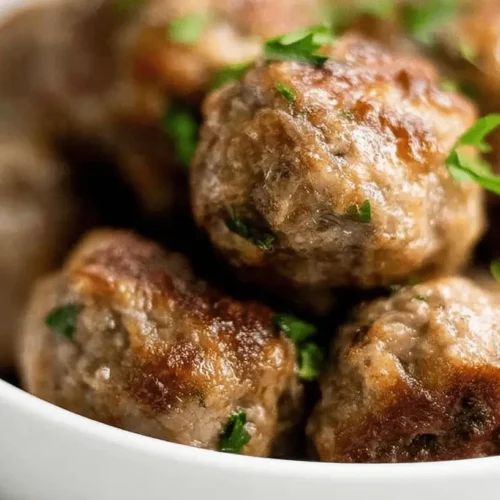 A close-up of a bowl brimming with freshly cooked, garnished homemade meatballs, perfect for a Homemade Meatballs Recipe.