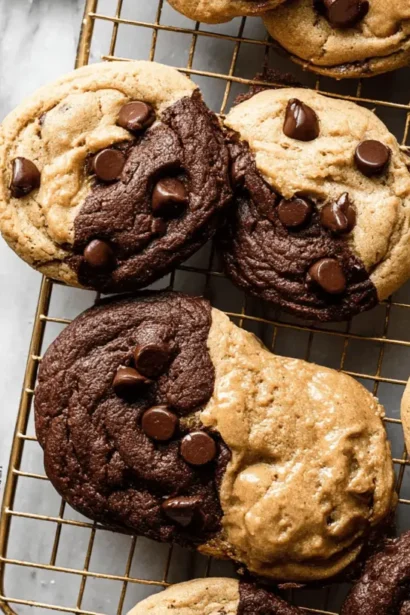 Freshly baked Peanut Butter Chocolate Swirl Cookies with two-toned halves and chocolate chips on a marble surface and cooling rack.