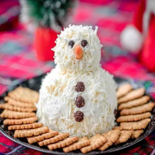 Festive Ranch Snowman Cheeseball, adorned with a top hat and facial features, served with crackers on a holiday plaid background.