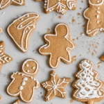 Festive gingerbread royal icing Christmas cookies, featuring various shapes like men, trees, and snowflakes, artfully decorated with white icing on a light countertop.