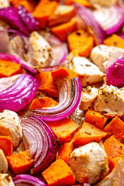 Vibrant close-up of Sheet Pan Chicken with Sweet Potatoes, red onions, and herbs on a rustic baking sheet.