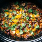 Overhead view of a hearty slow cooker cowboy casserole, rich with melted cheddar, beans, and cilantro, ready to serve.