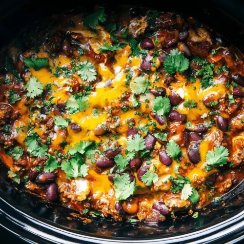 Overhead view of a hearty slow cooker cowboy casserole, rich with melted cheddar, beans, and cilantro, ready to serve.