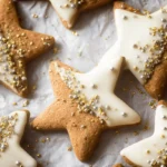 Delicious gold and silver sprinkled star cookies with creamy white icing on crinkled parchment paper.