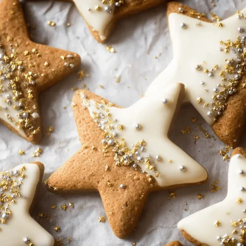 Delicious gold and silver sprinkled star cookies with creamy white icing on crinkled parchment paper.