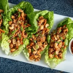 Beautifully plated Teriyaki Chicken Lettuce Wraps with carrots, cashews, and sesame seeds, served on a white dish with a side of dipping sauce.