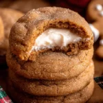 A close-up of delicious Christmas Gingerbread Cheesecake Cookies stacked with creamy filling, alongside a gingerbread man and a festive ornament.