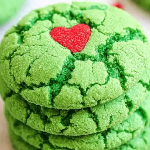 Vibrant stack of bright green Grinch Crinkle Cookies with a red heart, sparkling with sugar on a light surface.