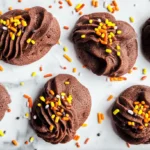 A flat lay of six Piped Chocolate Butter Cookies adorned with vibrant autumn-themed sprinkles on a white marble surface.