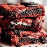 A close-up stack of three decadent Red Velvet Oreo Brownies with creamy filling and cookie pieces.