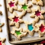 Vibrant star and snowflake-shaped stained glass window cookies on a baking sheet, perfect for holiday celebrations.
