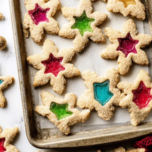 Vibrant star and snowflake-shaped stained glass window cookies on a baking sheet, perfect for holiday celebrations.