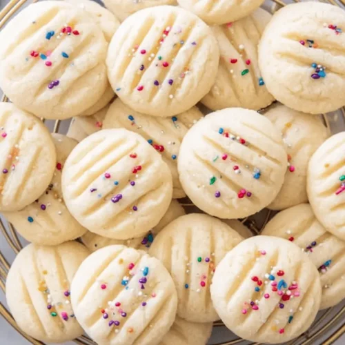 Overhead view of a gold basket filled with festive rainbow-sprinkled Whipped Shortbread Cookies and Christmas ornaments.